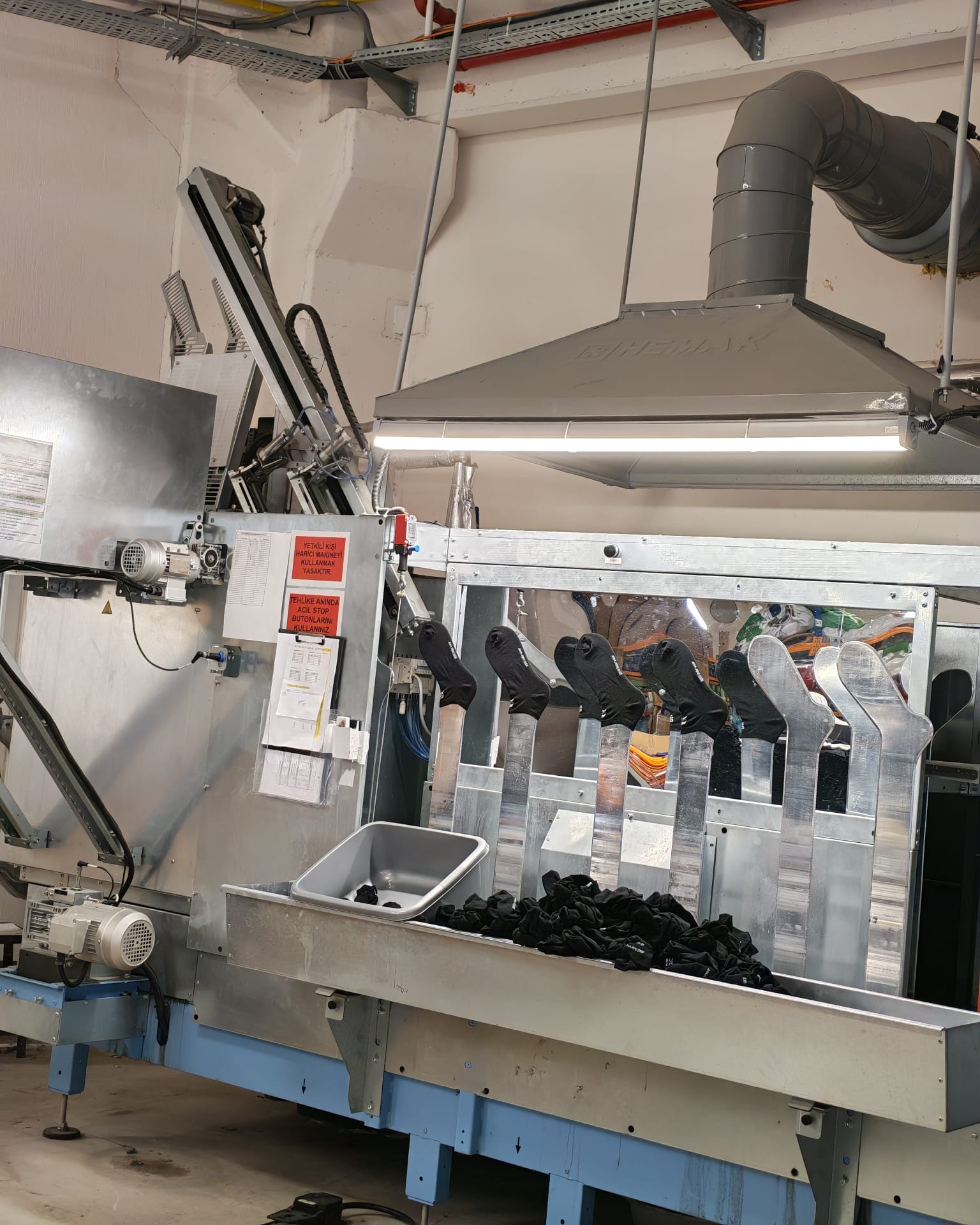 Tecnopea otomatik buharlı çorap ütü makinesi; metal kalıplarda ve teknede siyah çoraplar